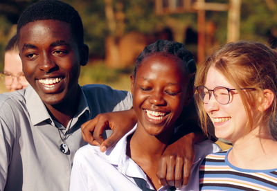 Foto: drei Jugendliche aus Afrika und Deutschland stehen zusammen, haben den Arm um die Schultern gelegt und lachen. 
