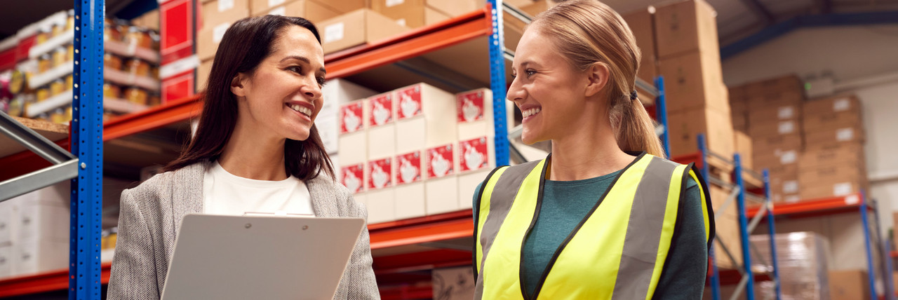 Foto: Ausbilderin im Bereich Logistik erkl&auml;rt einer Auszubildenden etwas neben einem Lagerregal.