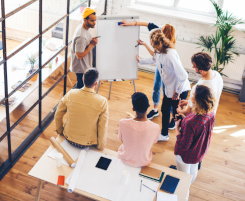 Foto: Eine Gruppe von Ausbilungspersonal oder Lehrkr&auml;ften steht im Kreis um ein FlipChart und erarbeitet gemeinsam eine Strategie.