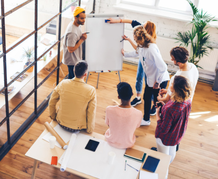 Foto: Eine Gruppe von Ausbilungspersonal oder Lehrkr&auml;ften steht im Kreis um ein FlipChart und erarbeitet gemeinsam eine Strategie.