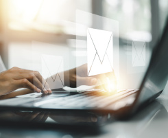 Foto: zwei H&auml;nde, die am Notebook eine E-Mail schreiben. Vor dem Bildschirm schwebt ein virtueller Briefumschlag.